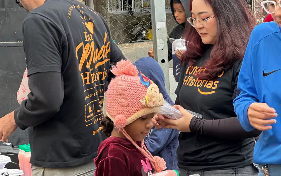 Voluntários de camiseta da Mudando Histórias entregam refeições para uma criança em uma ação de rua